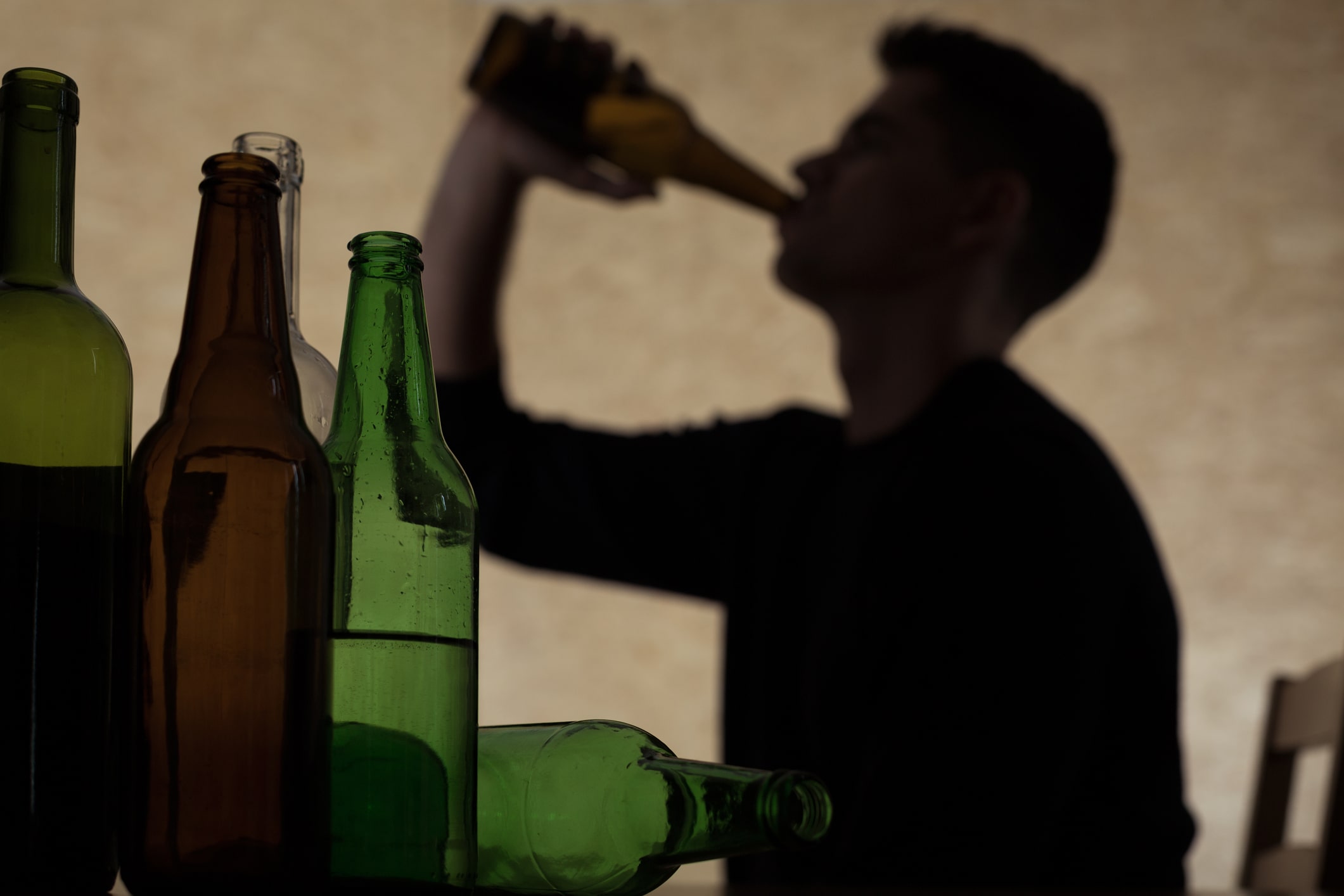man drinking too much alcohol with several empty bottles in foreground